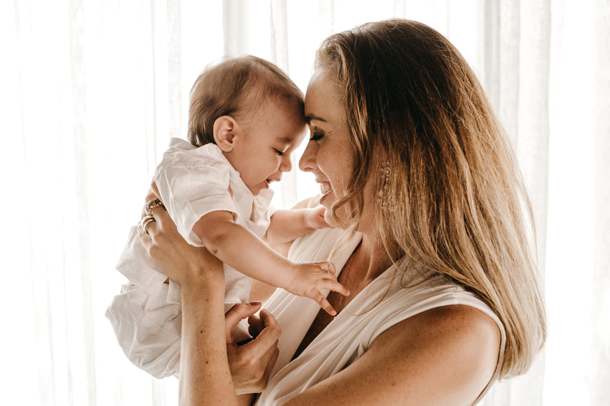 Una mamá levanta a su bebé y juntan sus frentes, sonriendo