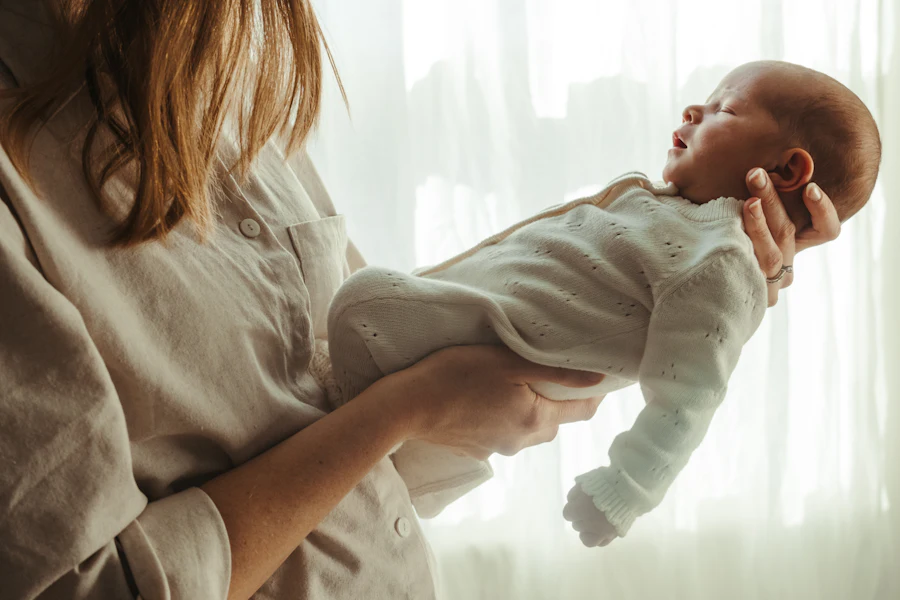 Una mamá sostiene a su recién nacido junto a una ventana